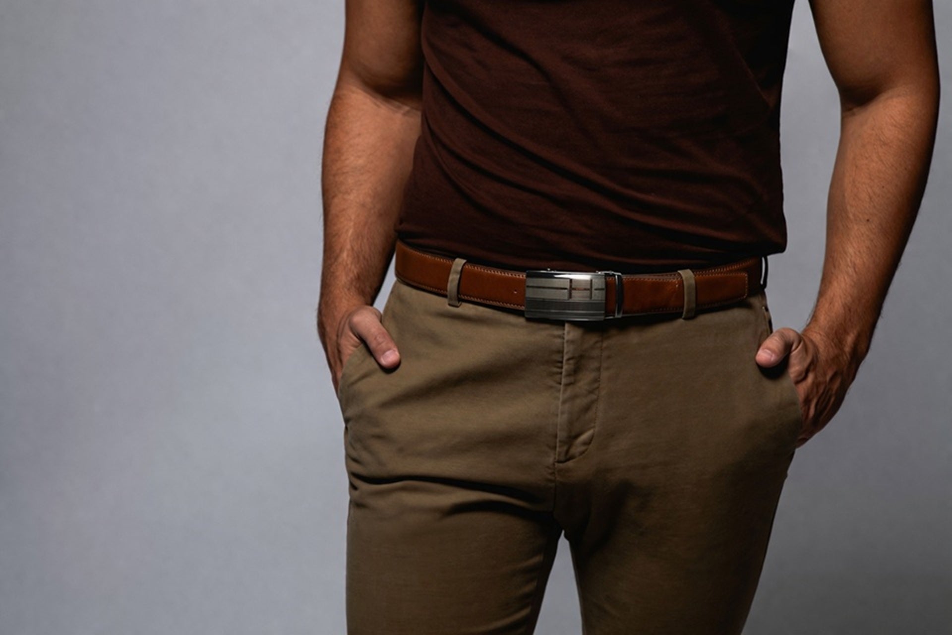 Man wearing a brown t-shirt and khaki pants with a belt on a gray background