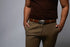 Man wearing a brown t-shirt and khaki pants with a belt on a gray background