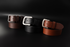 Three leather belts in brown, black, and red on a dark background
