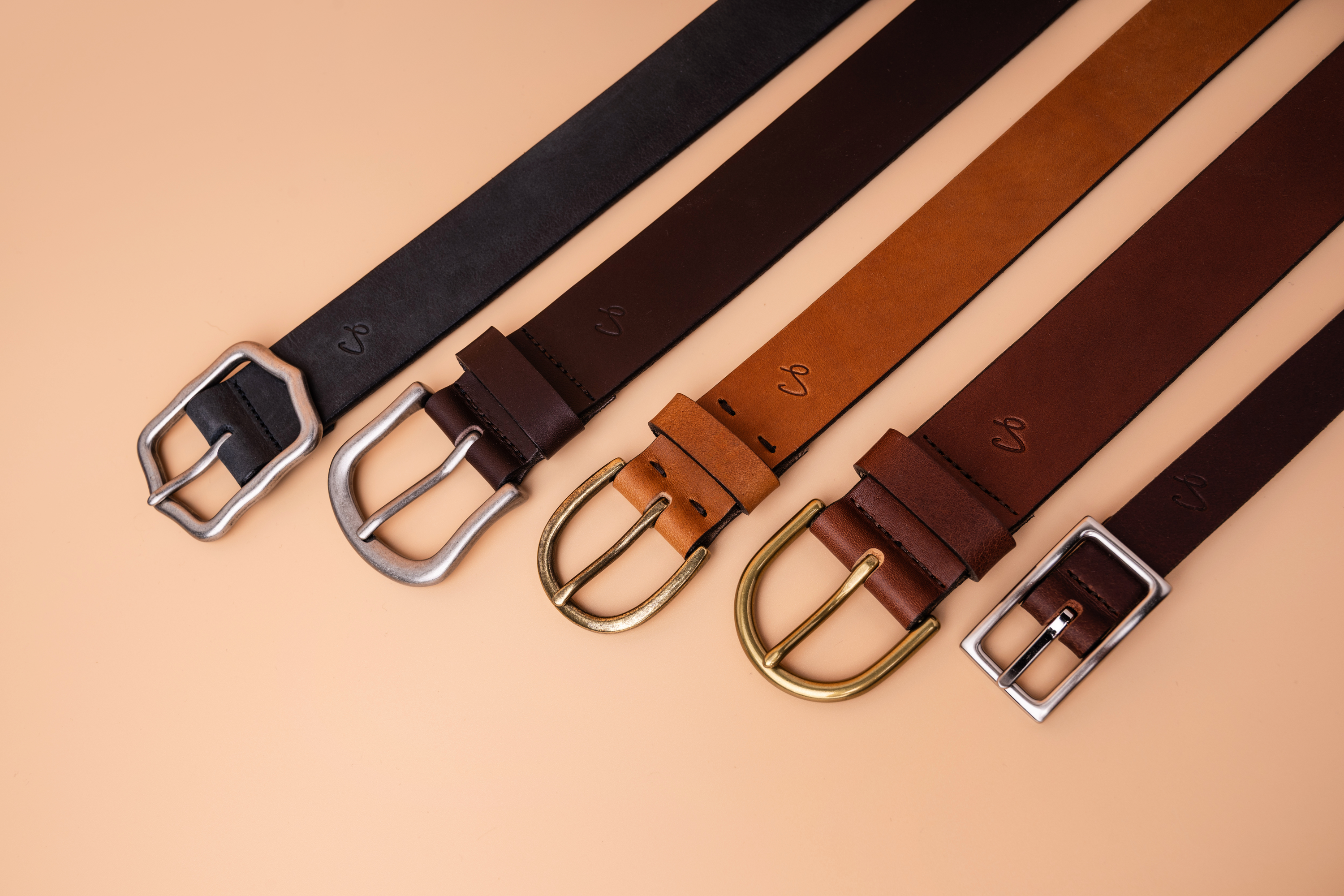 Four leather belts with different buckles on a beige background