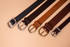 Four leather belts with different buckles on a beige background