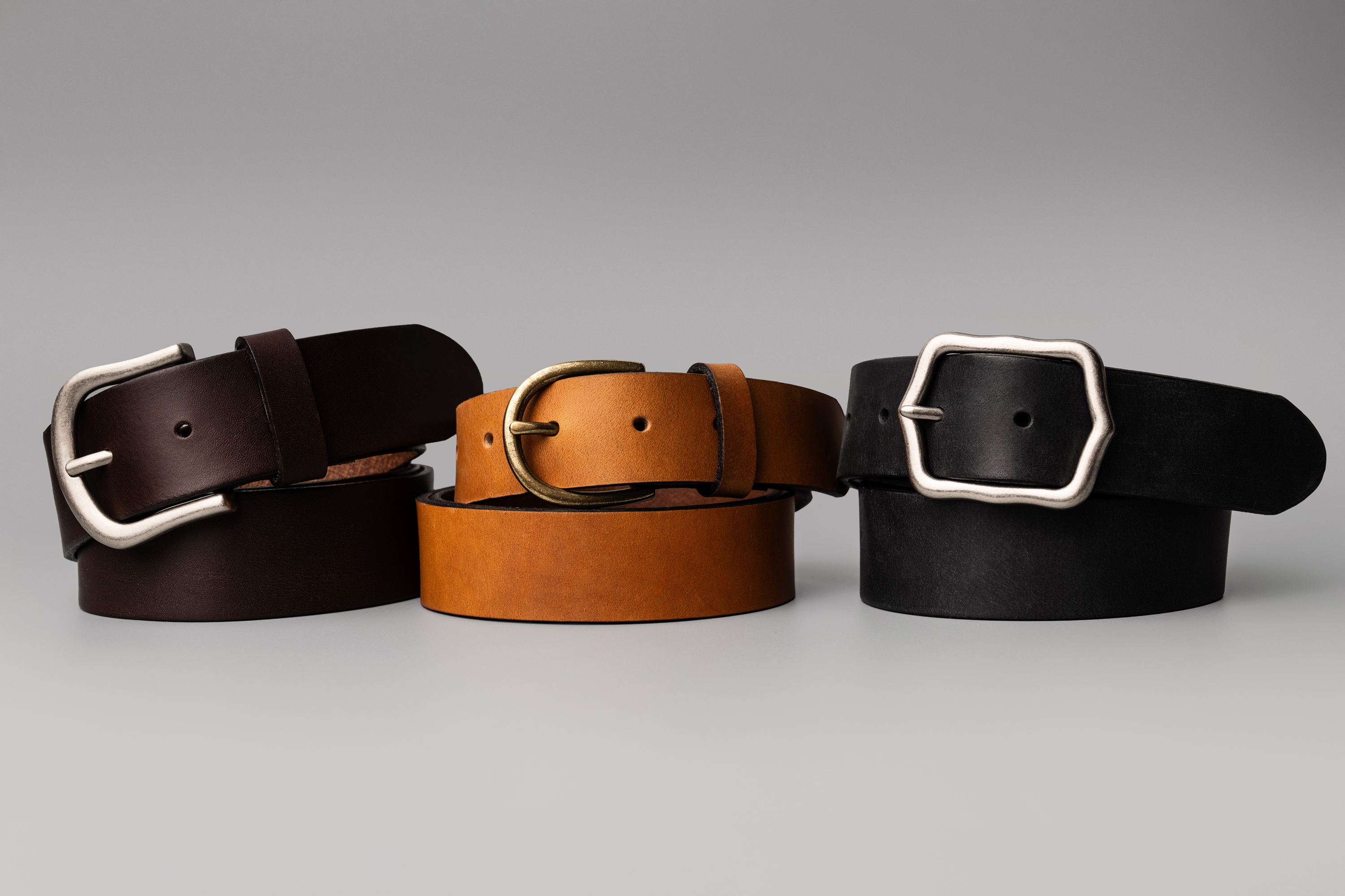 Three leather belts with silver buckles on a gray background