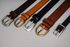 Four leather belts with different buckles on a gray background