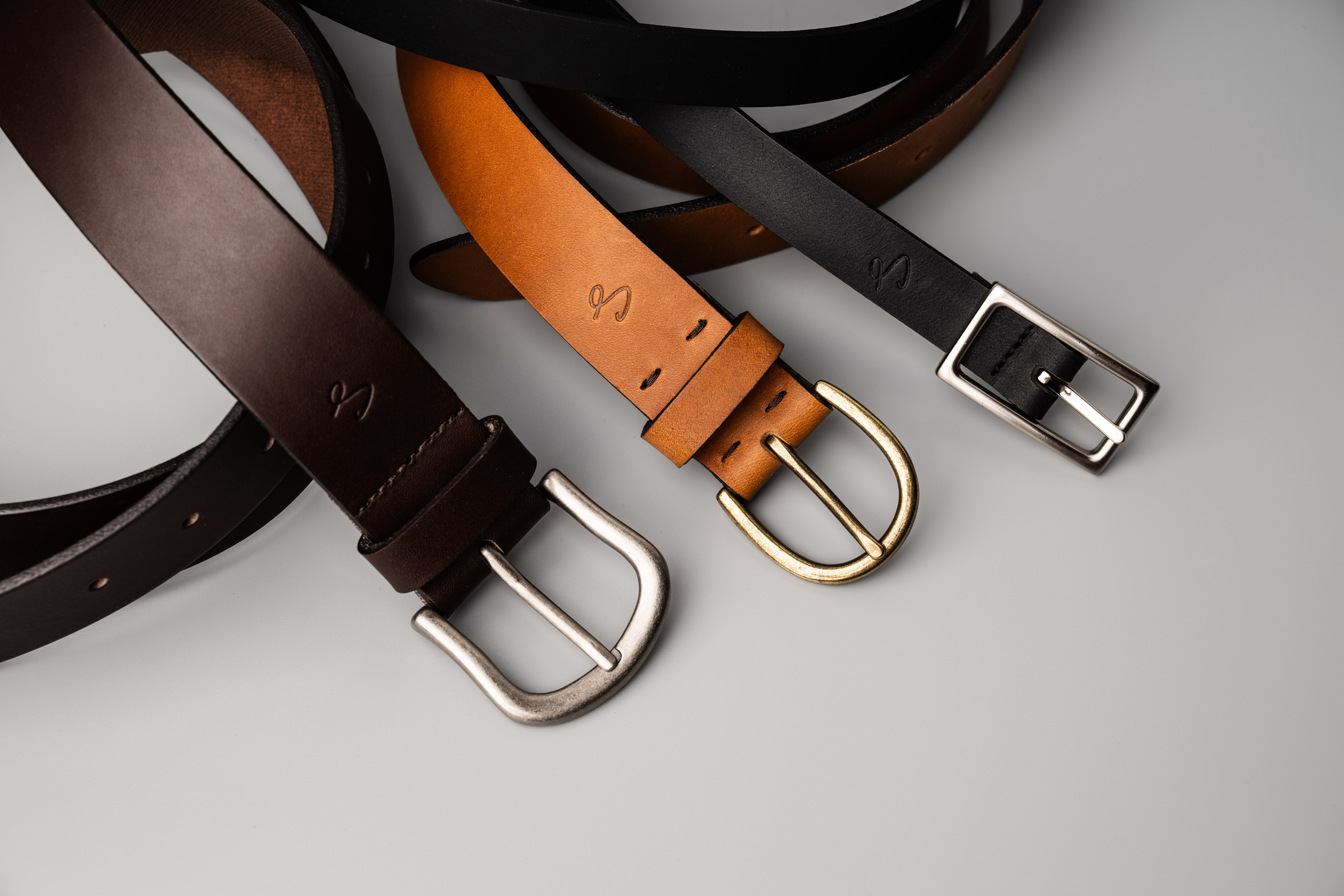 Three leather belts with different buckles on a light gray background
